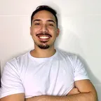 Rodrigo Souza, de camiseta branca e braços cruzados, sorrindo